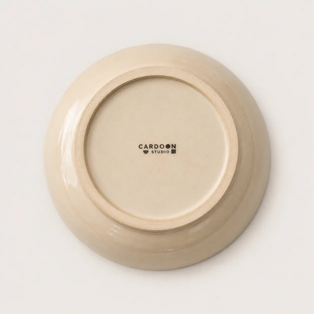 The underside of a round ceramic soup bowl in a warm cream-beige glaze, featuring the black printed brand name 'CARDON STUDIO' in the centre, set against a clean white background.