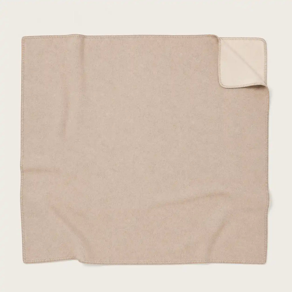 A folded beige throw blanket with a small corner turned up to show the reverse side, photographed on a plain light background.