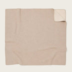 A folded beige throw blanket with a small corner turned up to show the reverse side, photographed on a plain light background.