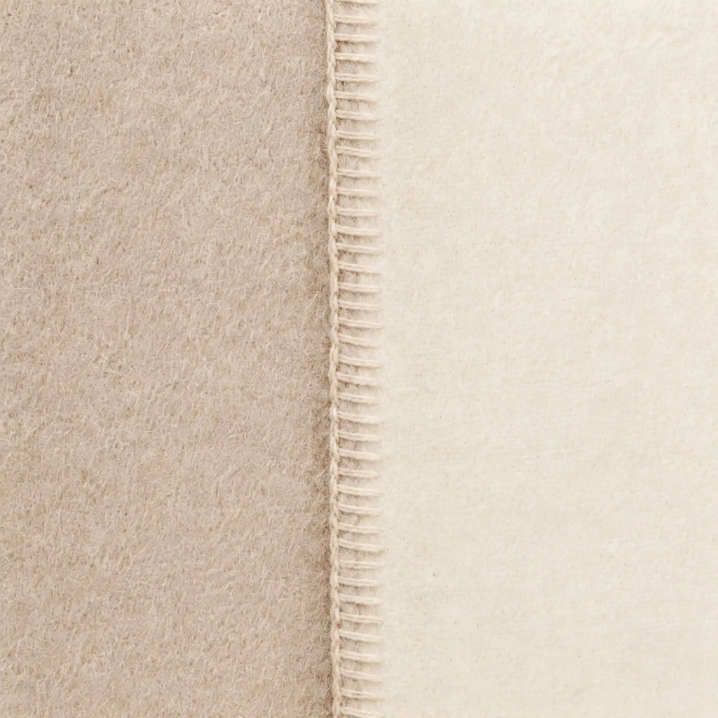 Close-up of a soft throw blanket in warm beige and cream tones, showing a stitched seam down the center.