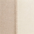 Close-up of a soft throw blanket in warm beige and cream tones, showing a stitched seam down the center.