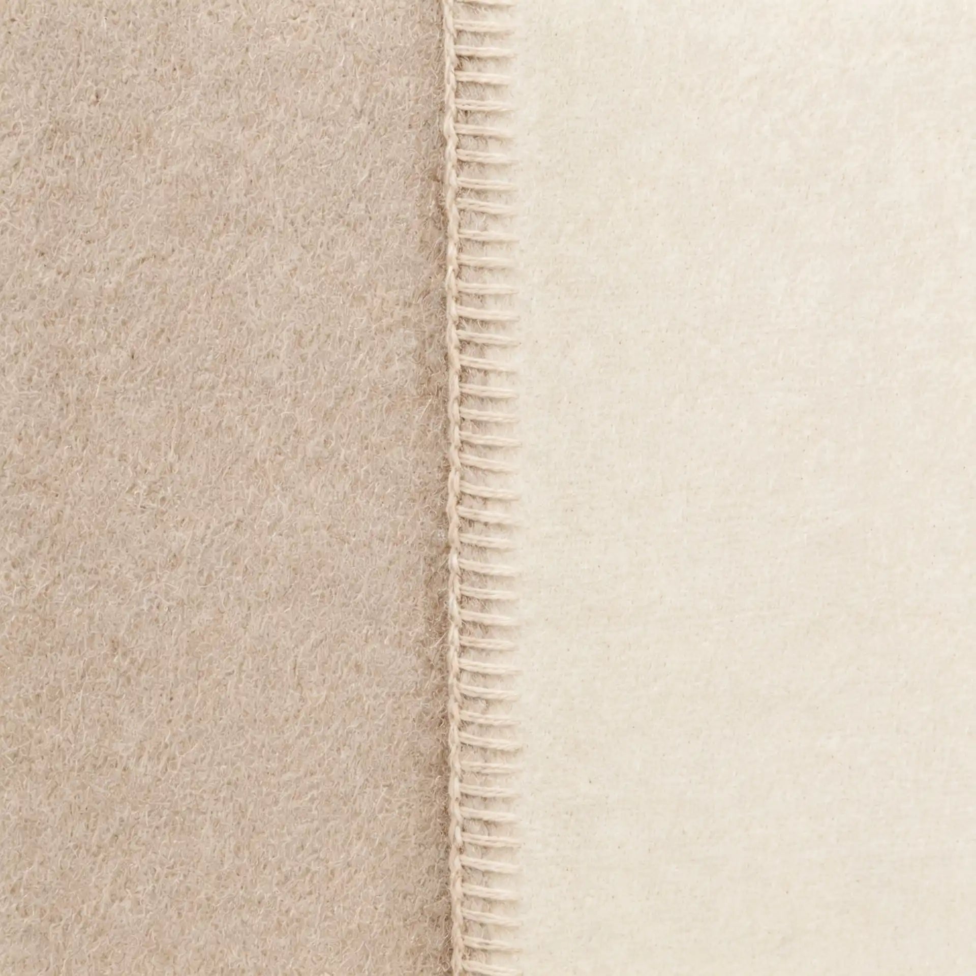Close-up of a soft throw blanket in warm beige and cream tones, showing a stitched seam down the center.