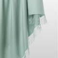 100% alpaca Solace Throw in Duck Egg Green colour. The woven textile drapes fluidly to showcase its airy texture, natural fibers, and minimalist design.