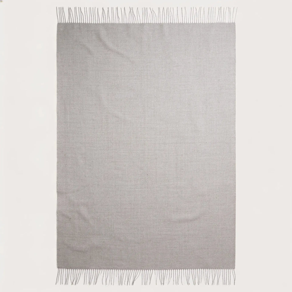 A light gray woven throw blanket with fringed edges, displayed flat against a solid off-white background.