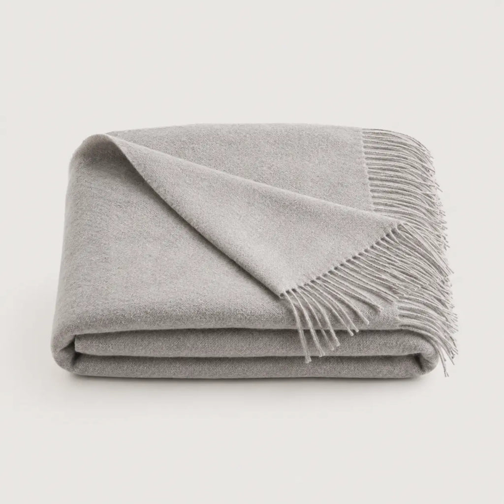 A folded light gray throw blanket with fringed edges, displayed on a clean off-white background.