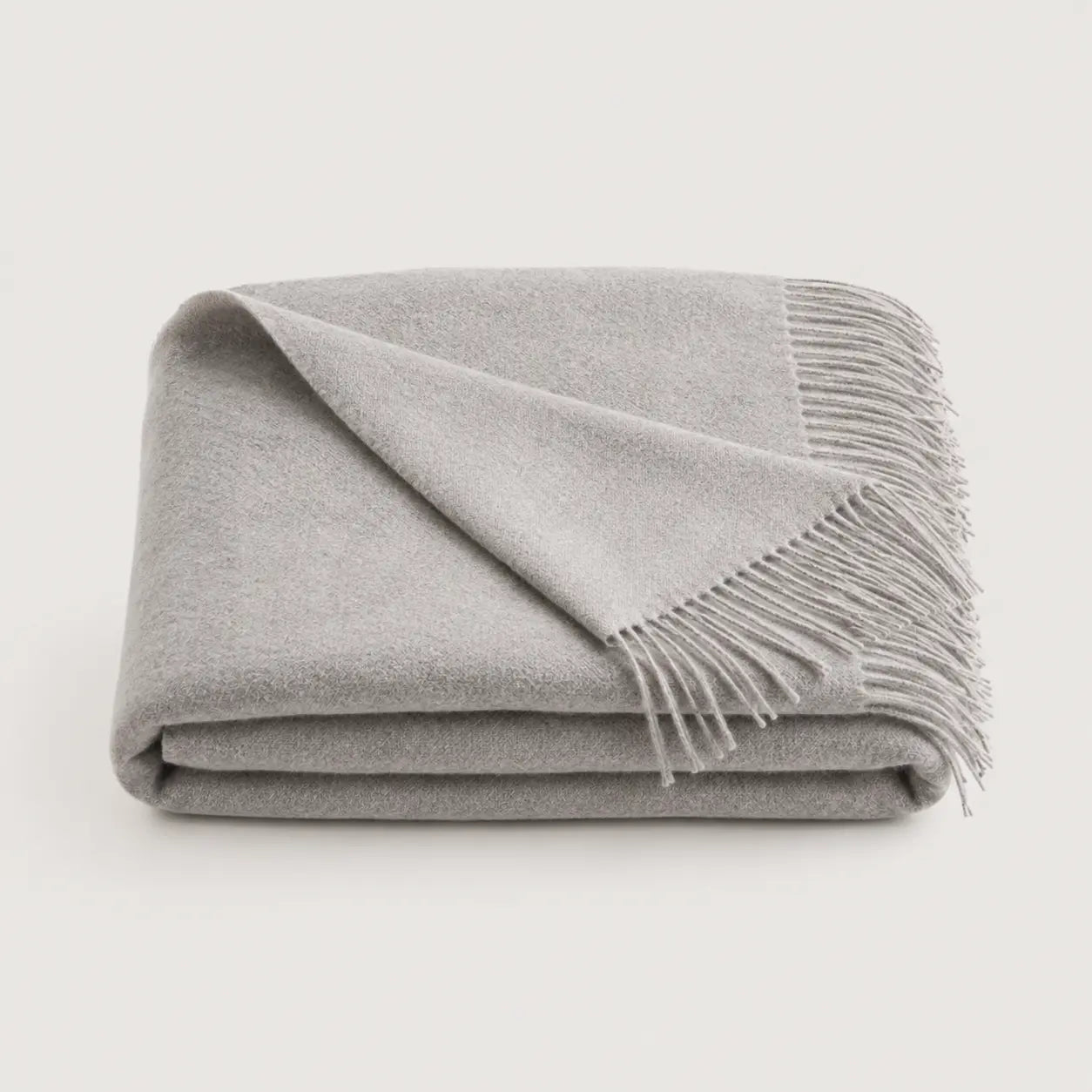 A folded light gray throw blanket with fringed edges, displayed on a clean off-white background.