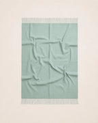 A square mint green throw blanket with white fringe on both ends, laid flat against a clean off-white background.