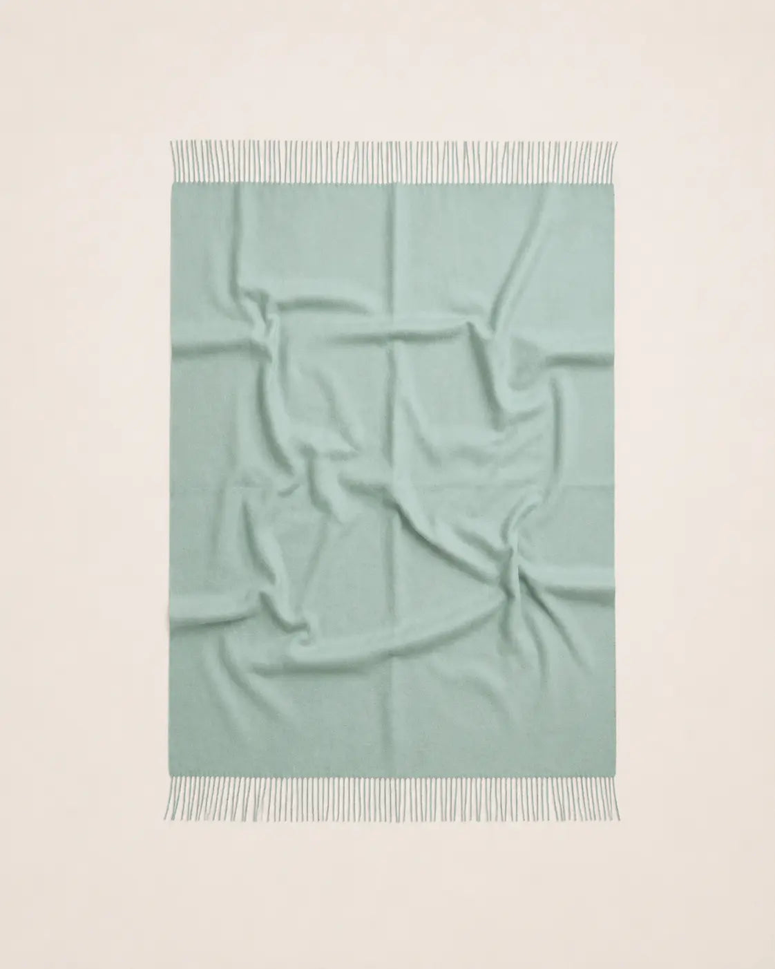A square mint green throw blanket with white fringe on both ends, laid flat against a clean off-white background.