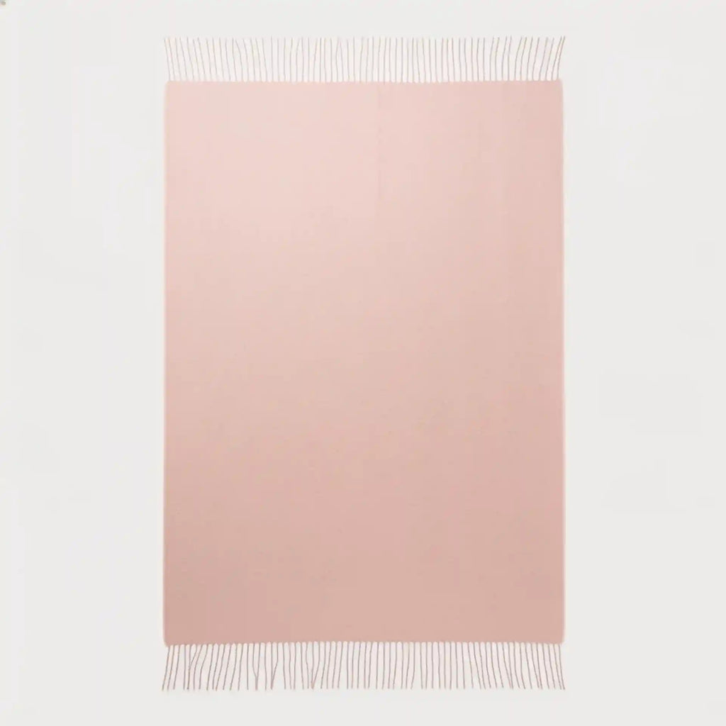 A rectangular blush pink throw blanket with fringed edges, displayed flat against a clean white background.