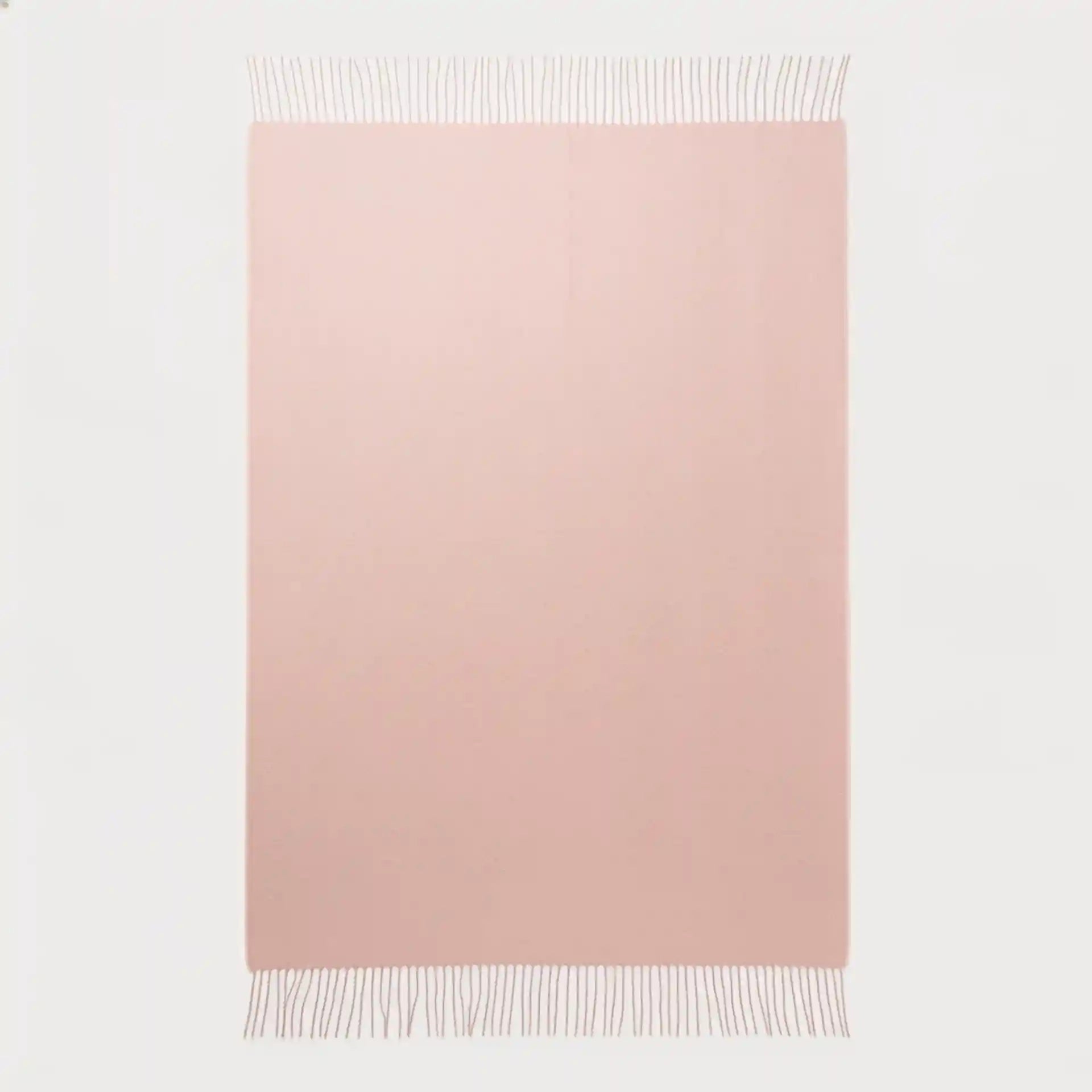 A rectangular blush pink throw blanket with fringed edges, displayed flat against a clean white background.