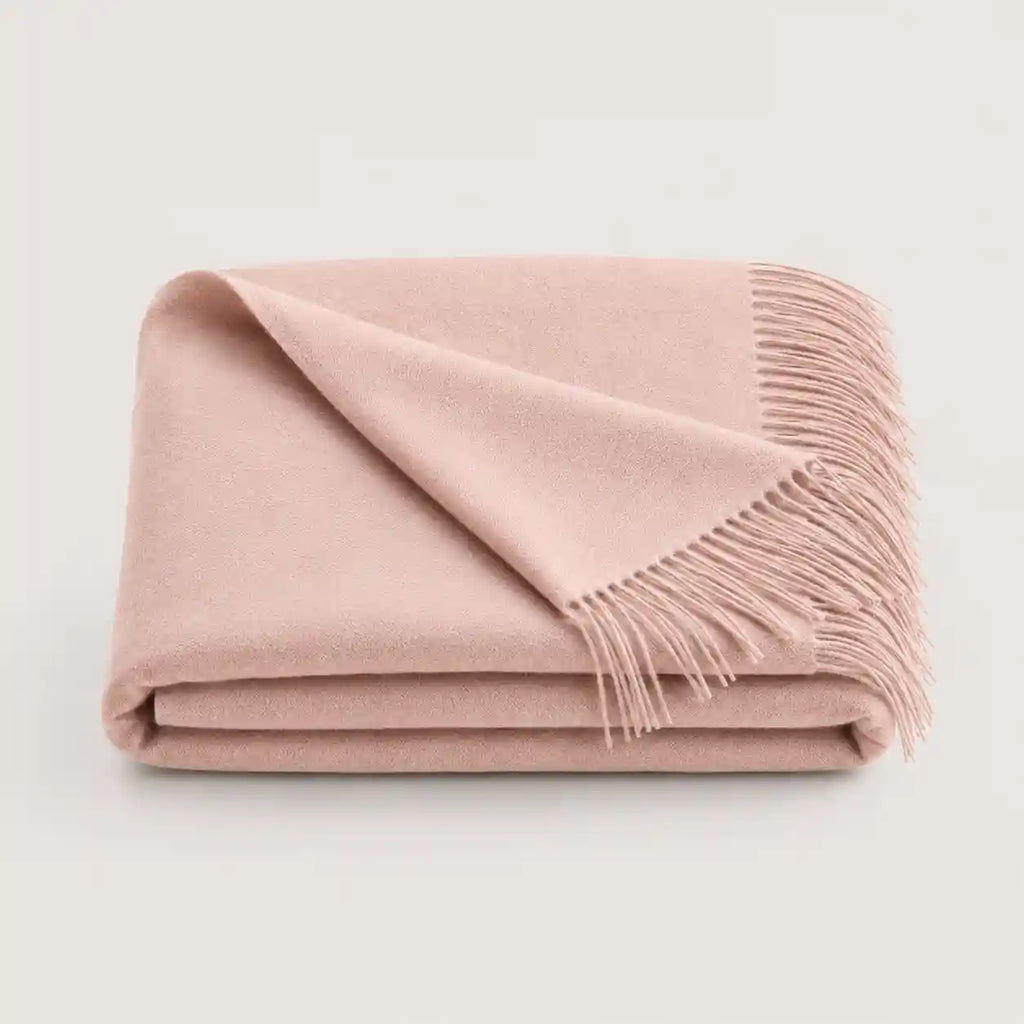 A folded dusty pink throw blanket with fringed edges, displayed on a clean, light off-white background.