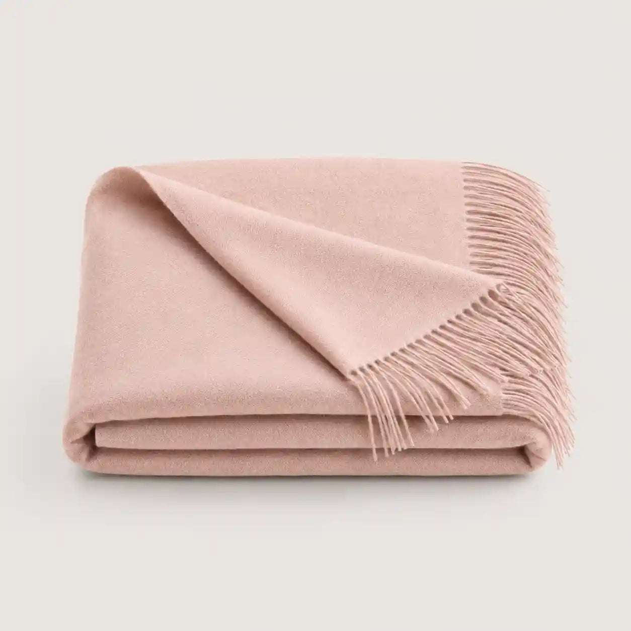 A folded dusty pink throw blanket with fringed edges, displayed on a clean, light off-white background.