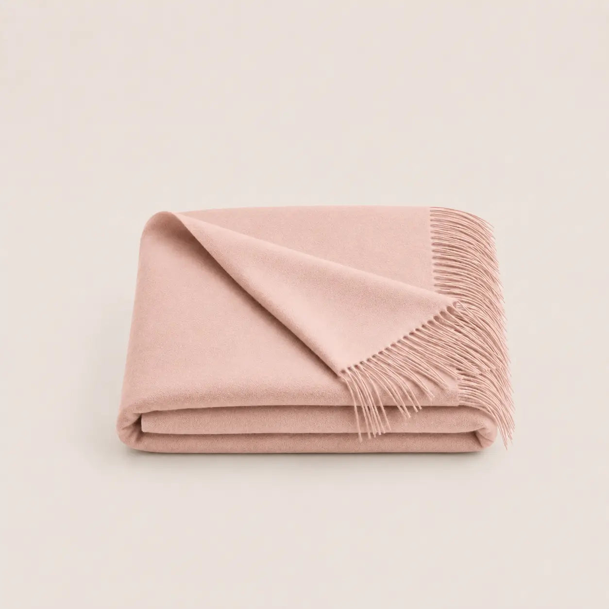 A folded dusty pink throw blanket with fringed edges, displayed on a clean, light off-white background.