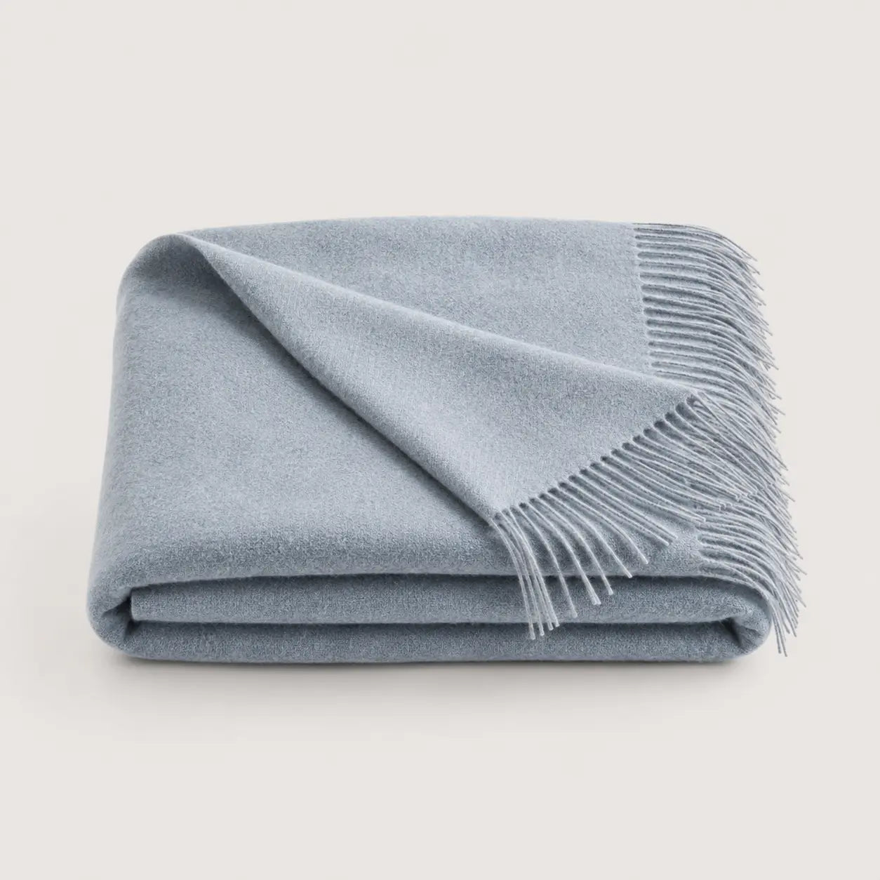 A folded light blue throw blanket with fringed edges, displayed on a clean, solid, light off-white background.