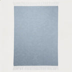 A rectangular light blue woven throw blanket with fringed edges, shown flat against a plain white background.