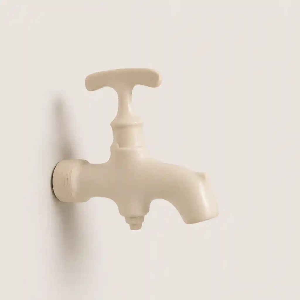 A single ceramic faucet with a T-shaped handle, shown mounted on a plain off-white wall.