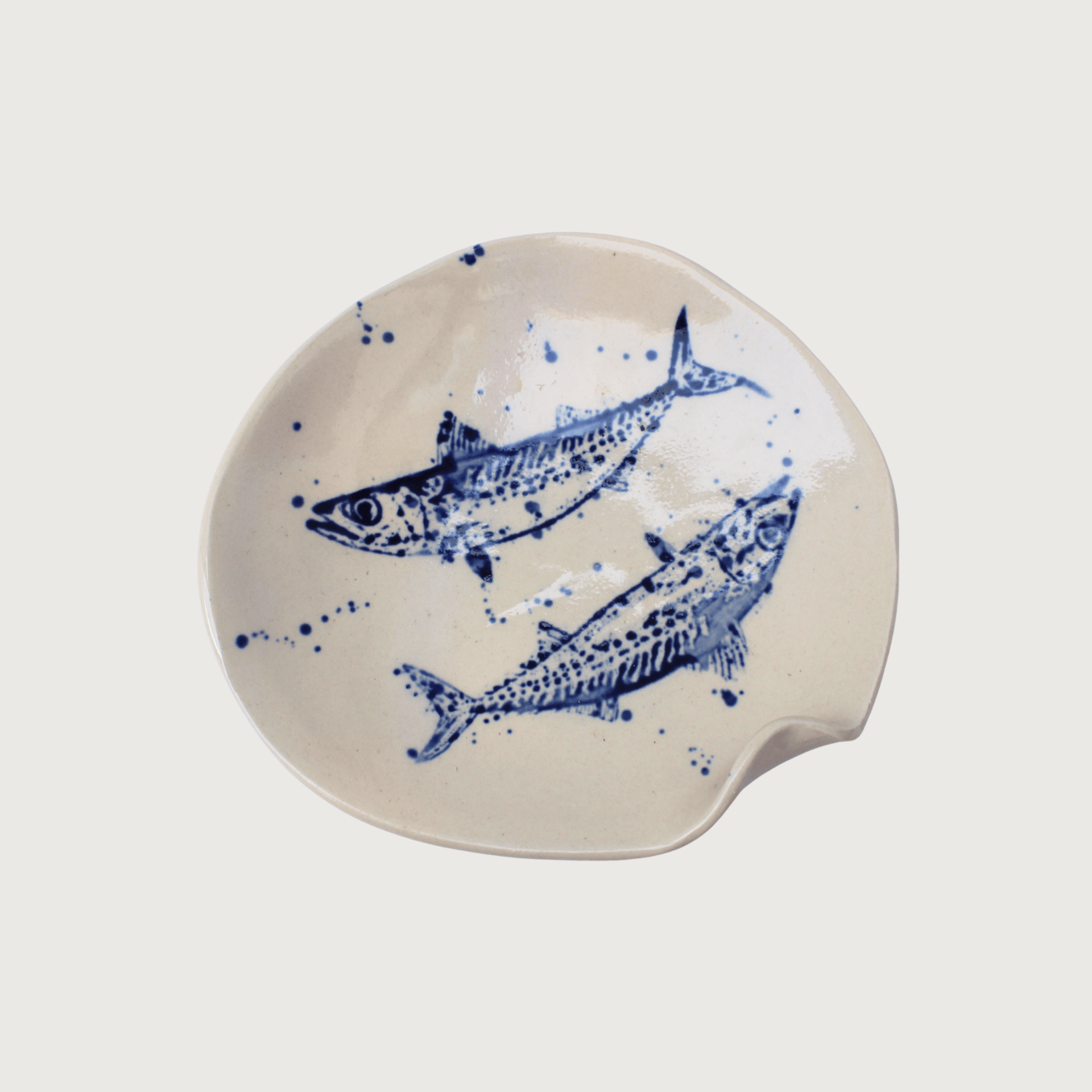 Handcrafted stoneware plate with blue hand-painted fish illustrations and organic asymmetrical shape. The ceramic serving plate features a cream glaze with artisanal detailing that showcases its coastal-inspired design and handmade finish.