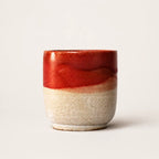 A small ceramic espresso cup with a glossy red top half and a speckled beige bottom half, photographed against a plain light background.