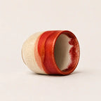 A handmade ceramic espresso cup with a textured cream exterior and a glossy red glazed finish, shown on a neutral light beige background.