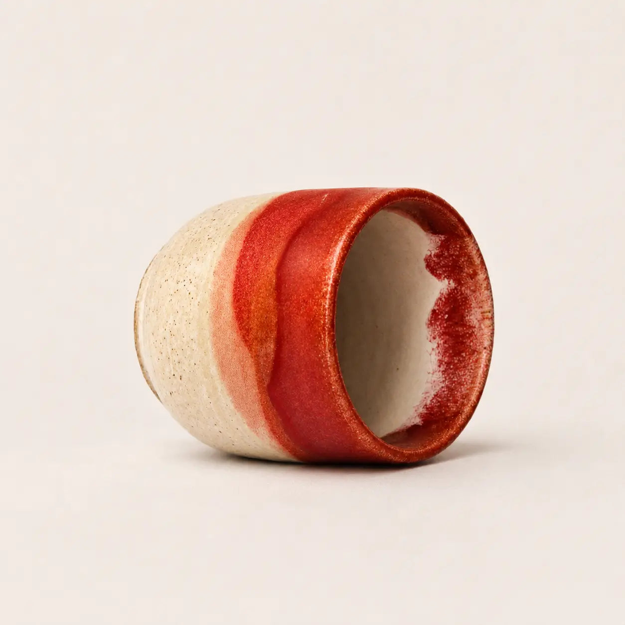 A handmade ceramic espresso cup with a textured cream exterior and a glossy red glazed finish, shown on a neutral light beige background.