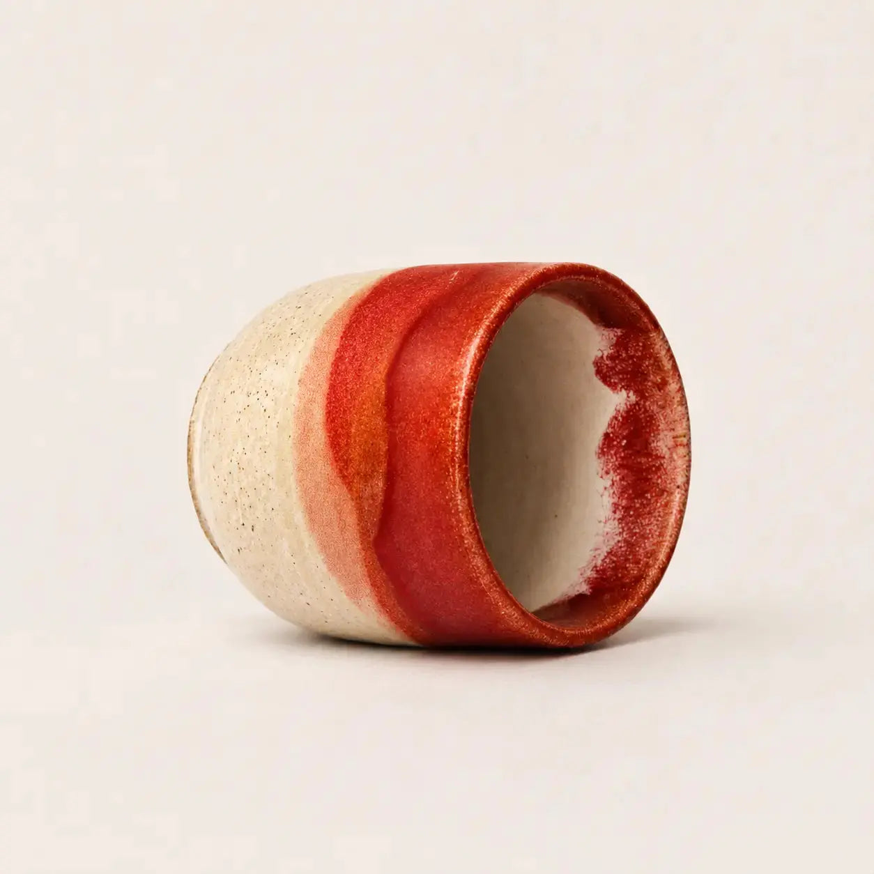 A handmade ceramic espresso cup with a textured cream exterior and a glossy red glazed finish, shown on a neutral light beige background.