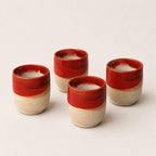 Four small ceramic espresso cups with a glossy red top half and a textured beige bottom half, arranged on a light beige background.
