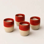 Four small ceramic espresso cups with a glossy red top half and a textured beige bottom half, arranged on a light beige background.