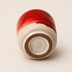 A ceramic espresso cup shown from its base, featuring a glossy deep red glazed top half and a speckled off-white clay bottom half with a brown terracotta ring around the foot.