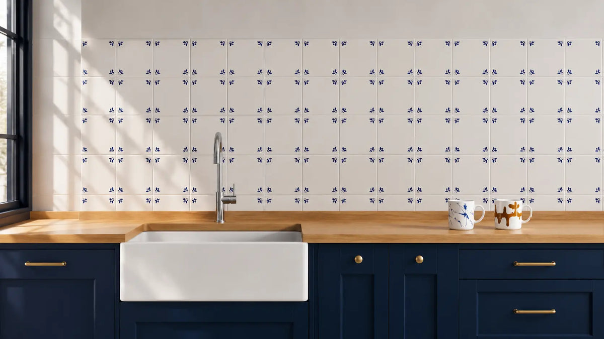 A kitchen backsplash featuring a repeating pattern of small blue floral tiles on a white background, installed above a light wood countertop with a white farmhouse sink and navy cabinets.