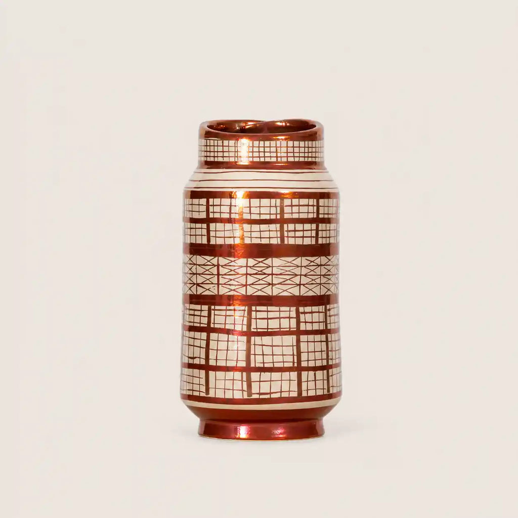 A small cylindrical ceramic vase with a glossy metallic copper-brown finish and a white grid pattern, set against a plain light beige background.