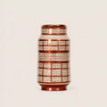 A small cylindrical ceramic vase with a glossy metallic copper-brown finish and a white grid pattern, set against a plain light beige background.