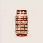 A small cylindrical ceramic vase with a glossy metallic copper-brown finish and a white grid pattern, set against a plain light beige background.