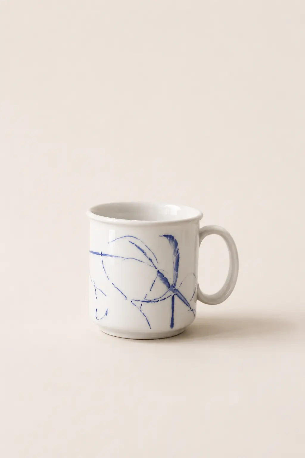 A white ceramic coffee mug with a blue abstract sketch design on the side, set against a solid beige background.