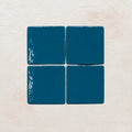 Four teal blue ceramic tiles on a textured beige surface