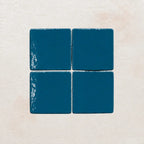 Four teal blue ceramic tiles on a textured beige surface