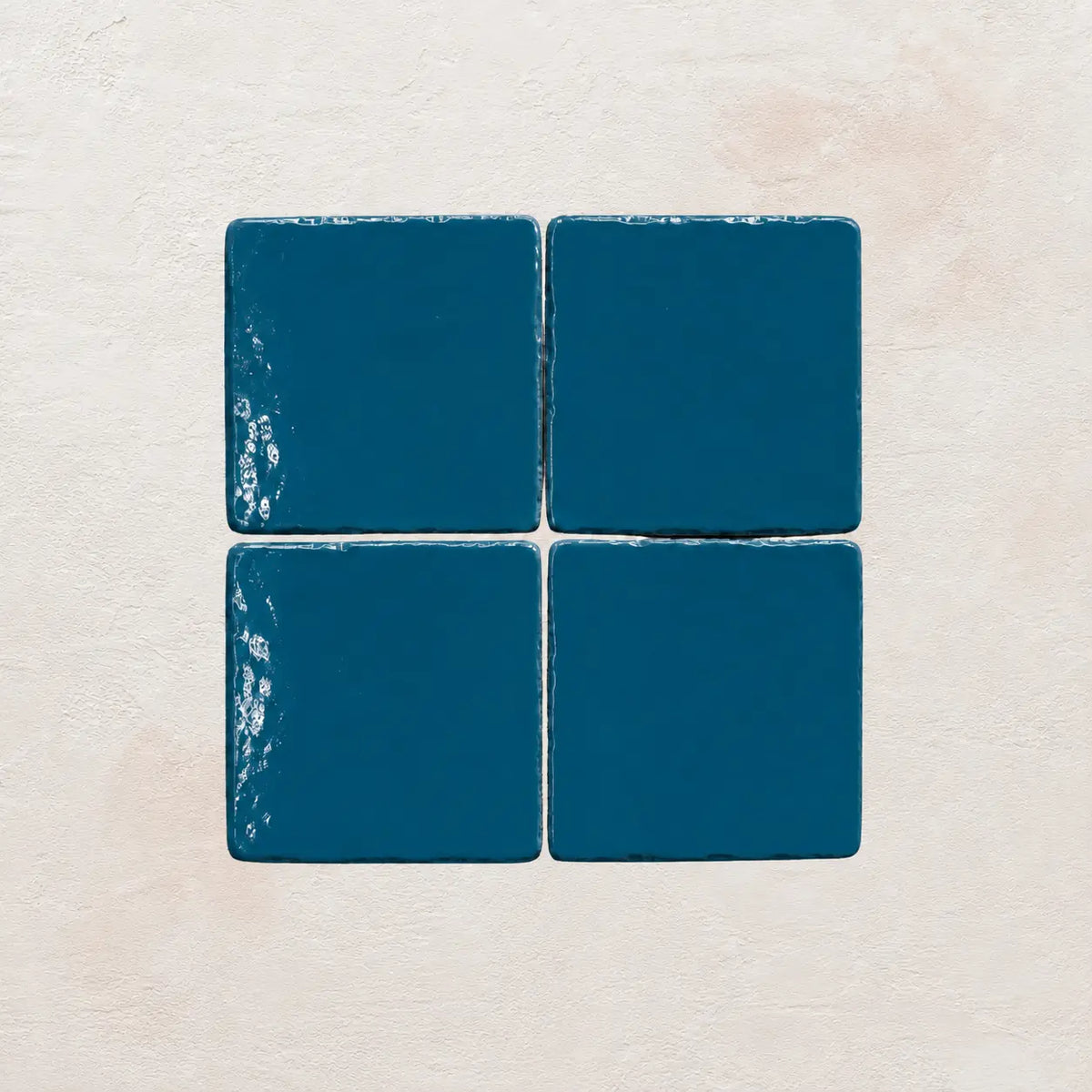 Four teal blue ceramic tiles on a textured beige surface