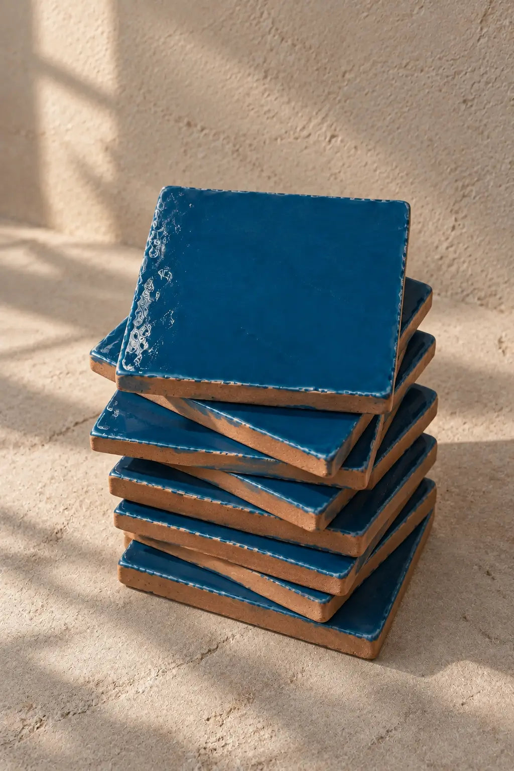 A stack of square teal blue coasters with a distressed, textured finish, photographed on a neutral beige textured background.