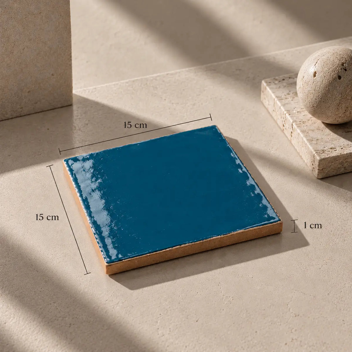 A square glossy blue ceramic tile with a natural wood edge, shown on a beige stone surface with dimension annotations indicating 15 cm by 15 cm and a 1 cm thickness.
