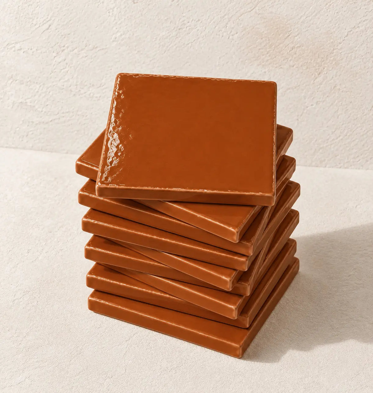 A stack of glossy square terracotta orange tile on a textured off-white background.