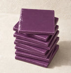 A stack of square violet ceramic tiles on a textured beige surface.