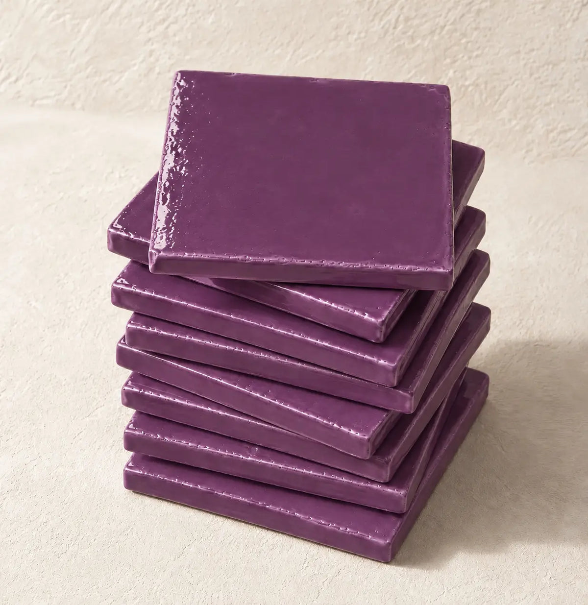 A stack of square violet ceramic tiles on a textured beige surface.