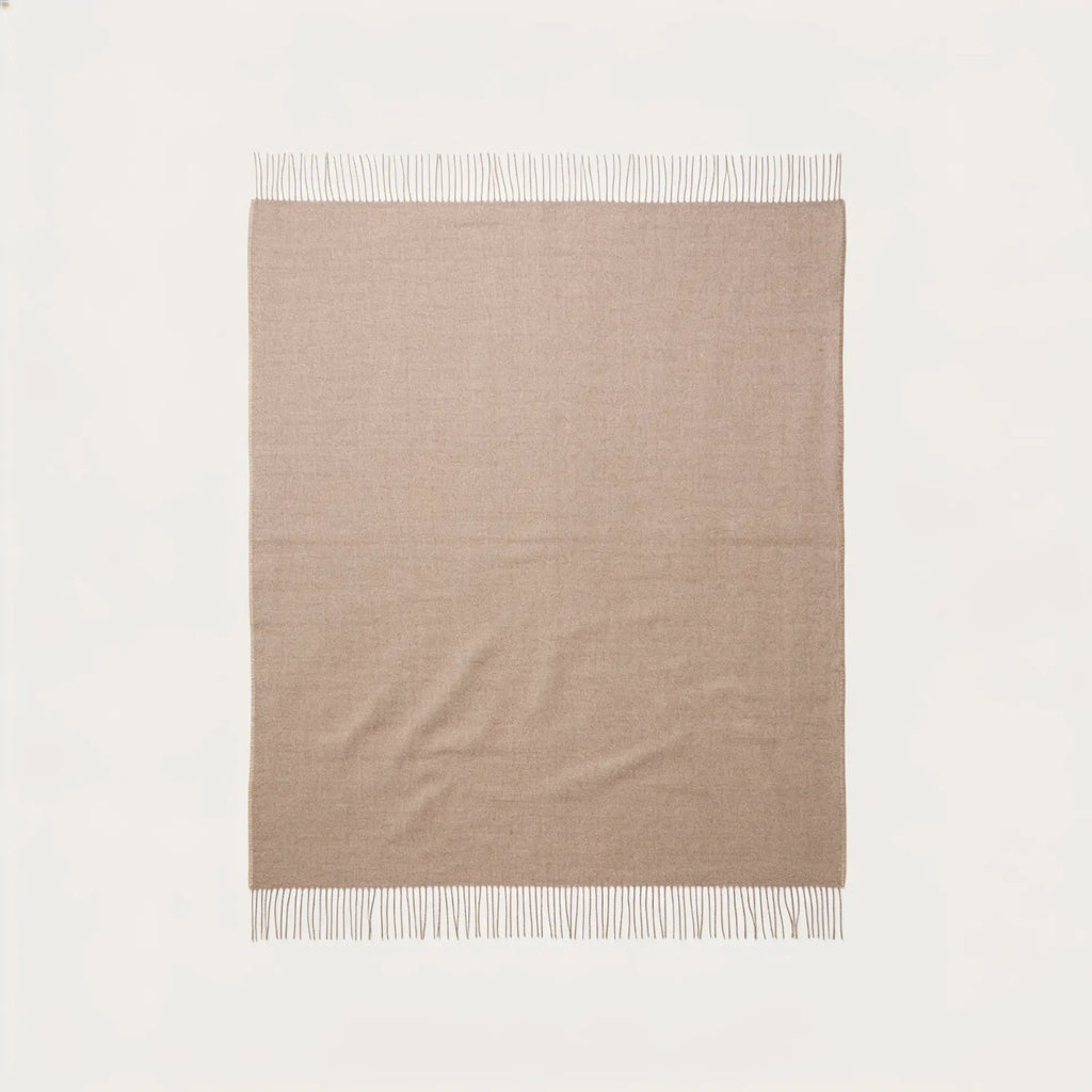 A rectangular beige throw blanket with fringed edges, laid flat against a clean off-white background.
