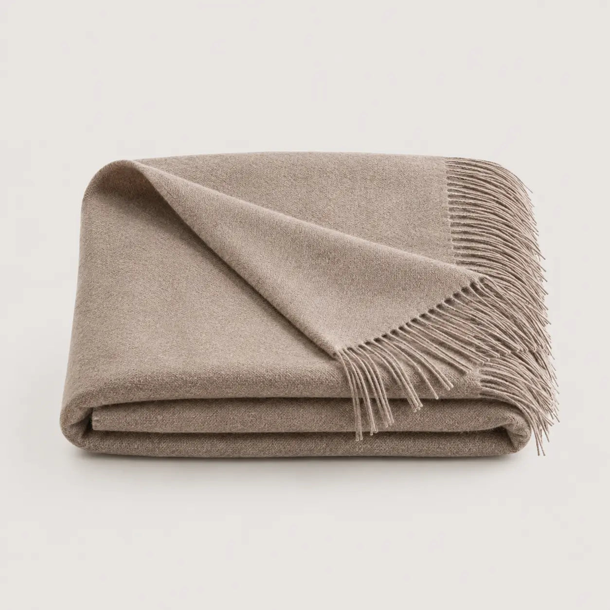 A folded beige throw blanket with fringed edges, displayed on a clean, light off-white background.