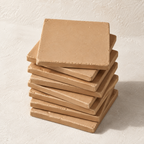 A stack of square tan ceramic coasters with a textured matte finish, photographed on a light beige textured background.