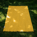 Yellow cashmere throw blanket on grass with sunlight filtering through leaves
