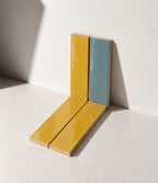 Glossy Saffron Yellow and Sky Blue handmade ceramic tiles arranged against a white wall in natural sunlight.