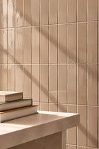 Beige rectangular wall tiles arranged in a grid pattern, with a light stone ledge in the foreground holding a stack of books and casting soft shadows.